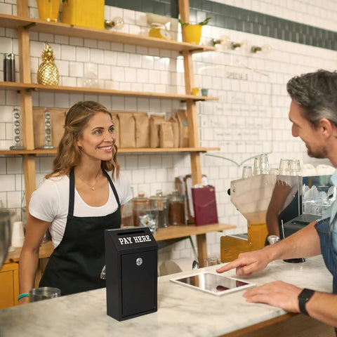 Locking Cash Box With Slot For Donations on cafe counter with barista serving customer, black metal money box