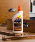 Carpenter Wood Glue Max bottle on table amid woodworking tools, showcasing extra-strength adhesive for interior and exterior use, 16 oz