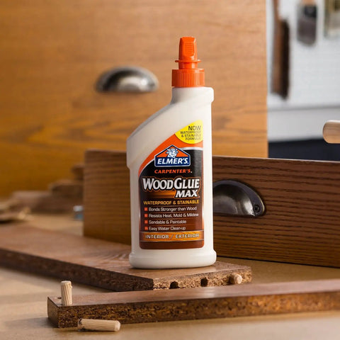 Carpenter Wood Glue Max bottle on table amid woodworking tools, showcasing extra-strength adhesive for interior and exterior use, 16 oz