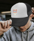 Man wearing a black and white cap with B-24 logo, grey hoodie, adjusting cap in an urban setting.