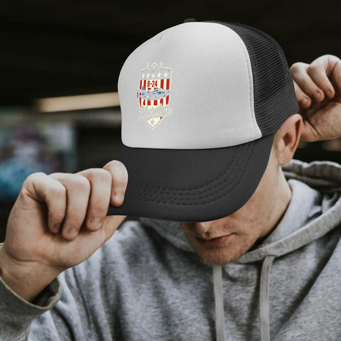 Man wearing a black and white cap with B-24 logo, grey hoodie, adjusting cap in an urban setting.