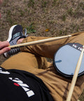 Six Inch Single Sided Practice Pad With Realistic Drumhead Feel And Low Volume For Quiet Jamming On The Go Natural Rubber On A Durable Wood Base To Train Wrists And Keep Your Chops Tight, shown on lap with sticks