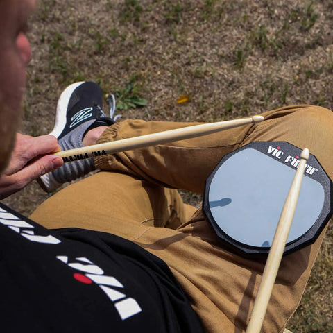 Six Inch Single Sided Practice Pad With Realistic Drumhead Feel And Low Volume For Quiet Jamming On The Go Natural Rubber On A Durable Wood Base To Train Wrists And Keep Your Chops Tight, shown on lap with sticks