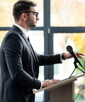 Man standing at podium with 800 Pcs Disposable Microphone Covers Non Woven with Elastic Band Individually Wrapped Mic Covers for KTV Karaoke Studio Recording Stage Black for Stage Use microphone cover on mic.