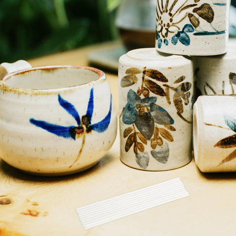 White ceramic pottery cups and jars with blue floral glaze on a wooden table; white ribbed strip in foreground