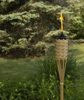 Single torch from Twelve Pack Bamboo Torches For Patio And Backyard 57 Inch Tall Weather Resistant Citronella Torches in garden setting.