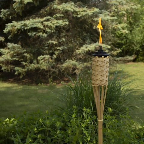 Single torch from Twelve Pack Bamboo Torches For Patio And Backyard 57 Inch Tall Weather Resistant Citronella Torches in garden setting.