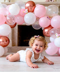 Balloon Arch Stand Kit with pink, white, and rose-gold balloons forming an arch behind a baby on the floor.