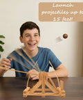 Leonardo Da Vinci Catapult Kit Build a Working Wooden Siege Engine in action, launching a projectile on a table with a child smiling