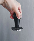 Hand holding Spring Loaded Espresso Tamper 53.3mm with ripple base and anodized aluminum handle, showcasing ergonomic design.