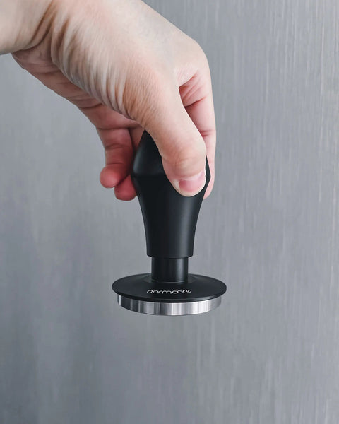 Hand holding Spring Loaded Espresso Tamper 53.3mm with ripple base and anodized aluminum handle, showcasing ergonomic design.