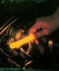Hand holding Orange Glow Sticks 6 Inch Emergency ChemLight Glow Sticks With 12 Hour Brightness next to machinery in dark