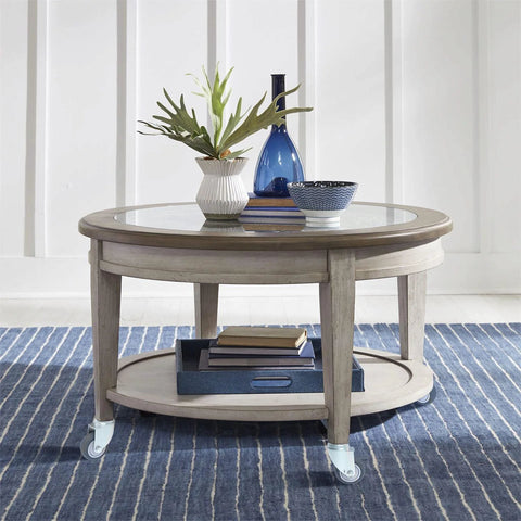 Round glass-top coffee table on four swivel caster wheels with a light gray wood frame.