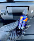 CARPRO DLUX wheel and trim coating bottle (blue with orange label) held by a gloved hand in front of a car tailgate.