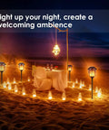 Solar Torch Lights Outdoor Flickering Flame Lit Set Of 4 Metal Pathway Lights surrounding a beachside table setting at night.