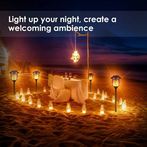 Solar Torch Lights Outdoor Flickering Flame Lit Set Of 4 Metal Pathway Lights surrounding a beachside table setting at night.