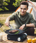 Man cooking steak on Grab And Go Portable Butane Camping Stove With Carrying Case Precise Heat Control For Patio Cooking
