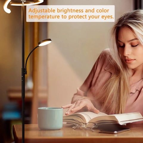 Lit LED Floor Lamp With Rotatable Main Light And Flexible Reading Light next to woman reading book with remote on table