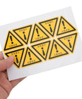 Hand holding a sheet of 24 Pack Yellow PVC Caution Sign Stickers For Machines And Gear That Last Long Easy To Stick Durable Warehouse
