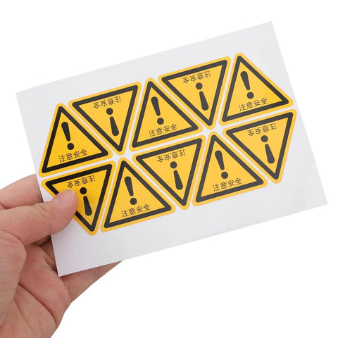Hand holding a sheet of 24 Pack Yellow PVC Caution Sign Stickers For Machines And Gear That Last Long Easy To Stick Durable Warehouse