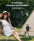 Portable Camping Fan With LED Lantern, 360 Degree Rotating Head on a table beside a tent, woman seated nearby.