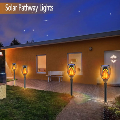 8 Pack Solar Torch Lights With Real Flickering Flame illuminating a walkway by a house, creating a warm nighttime ambiance.
