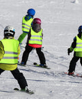 Kids wearing green reflective safety vests with zipper skiing on snowy day, demonstrating kids reflective safety vest 20 pack.
