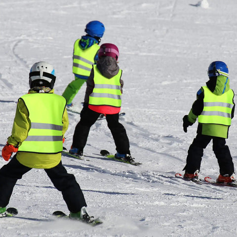 Kids wearing green reflective safety vests with zipper skiing on snowy day, demonstrating kids reflective safety vest 20 pack.
