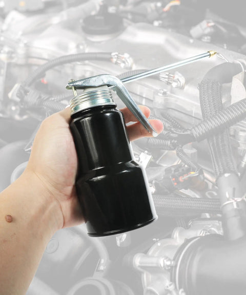 Hand holding Badass Heavy Duty Metal Pump Oil Can With Comfort Grip Pistol Handle and Six Inch Spout near an engine.