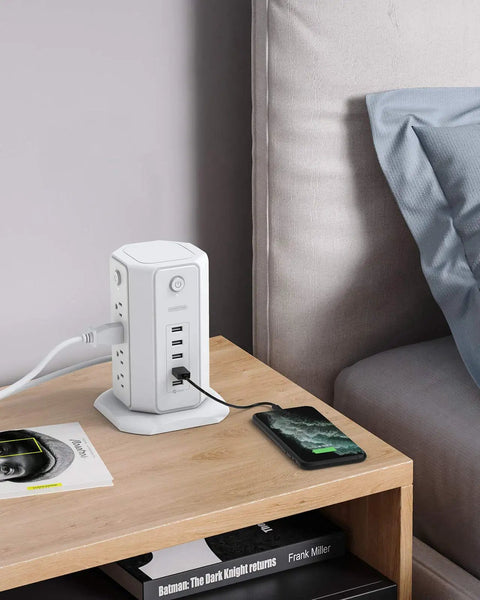 8-Outlet Tower Surge Protector With USB Charging Station on bedside table in home office setting, charging phone, 6-foot flat plug.