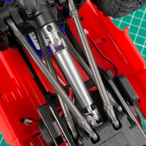 2 Pack Steel CVD Driveshafts For 1 To 18 TRX4 M K10 F150 RC Crawler Upgrades Silver Beefy Heavy Duty Connection For Smooth Power Transfer And Precision Fit Ideal RC Crawler Upgrade For Stability And Durability. Installed steel RC crawler driveshafts under red chassis.