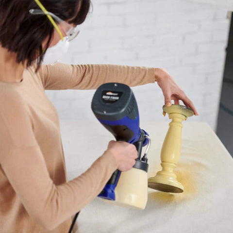 Woman using Quick Finish HVLP Paint Sprayer for Crafting and Furniture on a small yellow candlestick, applying smooth even coat.