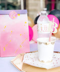 Tie Dye Party Favor Bags With 36 Stickers 30 Pack Mermaid Unicorn Themed Goodie Bags next to birthday cup and plate on table.