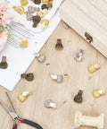 Dope Antique Zinc Alloy Feet Set 30 Pieces In 3 Colors scattered on a wooden table with tools and flowers.