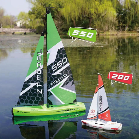 Two 1:22 Scale Wind Powered RC Racing Sailboats on a pond, green and white hull with mast and sails attached, trees in background