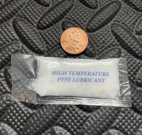 Small packet labeled 'High Temperature PTFE Lubricant' next to a coin on textured surface.