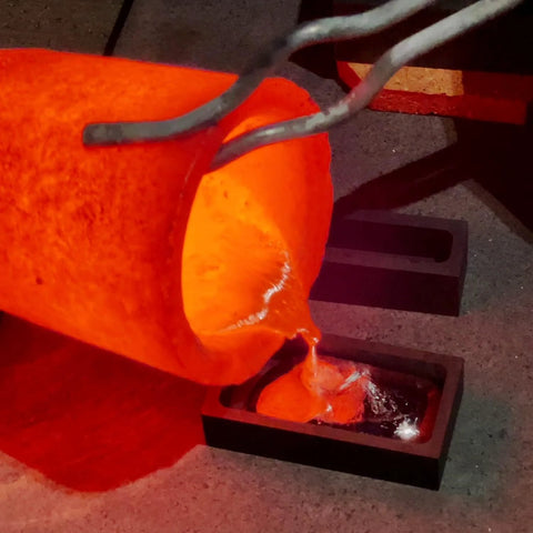 Graphite ingot molds for metal casting; glowing molten orange metal pours into two rectangular molds.