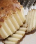 Crinkle cutter knife with wood handle slicing a potato into ridged slices.