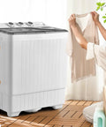 Compact Twin Tub Portable Washing Machine With Separate Wash And Spin Dryer Dual Timer Knobs Auto Drain Pump Fits Any Small Room Light Grey White in use with a person holding a shirt.