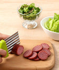XLIUAX crinkle cutter with green handle and stainless wavy blade slicing sausage on a wooden cutting board