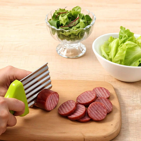 XLIUAX crinkle cutter with green handle and stainless wavy blade slicing sausage on a wooden cutting board