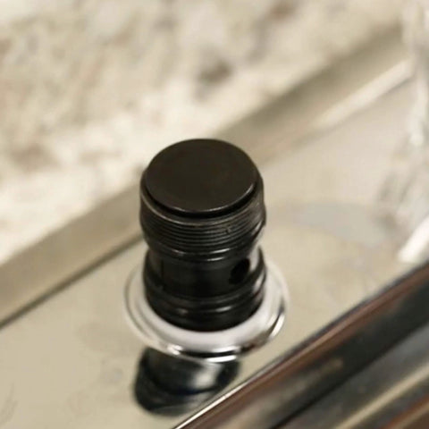 Danco faucet grease cap, black plastic, mounted on chrome faucet stem, close-up view.