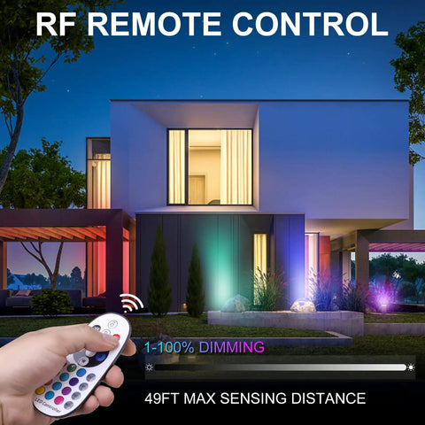 Person using remote control for Eight Pack RGBW Landscape Lights For Outdoors, illuminating modern house at night with colored lights.