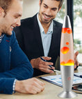 13 Inch Liquid Motion Lamp With Yellow Wax Flow In Clear Water on a desk with people around, creating a cozy vibe in an office setting