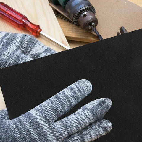 Hand in striped glove holding a black wet dry sanding sheet from the Twenty Pack Of Premium Wet Dry Sanding Sheets 11x9 Inch Assortment.
