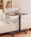 Compact Standing Desk On Wheels With Foldable 24 Inch Desktop Lockable Casters Adjustable Height From 25 To 36.5 Inches Ideal Overbed Or Home Office Laptop Table In Walnut Finish used by a person on a sofa