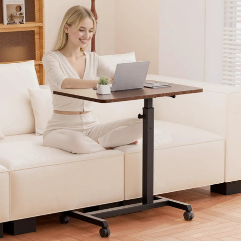 Compact Standing Desk On Wheels With Foldable 24 Inch Desktop Lockable Casters Adjustable Height From 25 To 36.5 Inches Ideal Overbed Or Home Office Laptop Table In Walnut Finish used by a person on a sofa