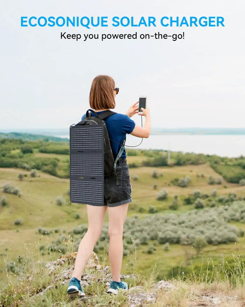 Person using phone with 30W Portable Solar Panel Charger With All In One Foldable Tri Fold Design attached to backpack in scenic field