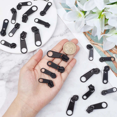 Zipper Puller Replacement Kit 32 Pieces In Four Sizes Quick Fix Zipper Slider Set displayed in hand next to a coin for scale.