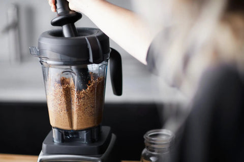 Person using Low Profile Tamper for 64-ounce container with BPA-free plastic design, blending thick mixture on counter